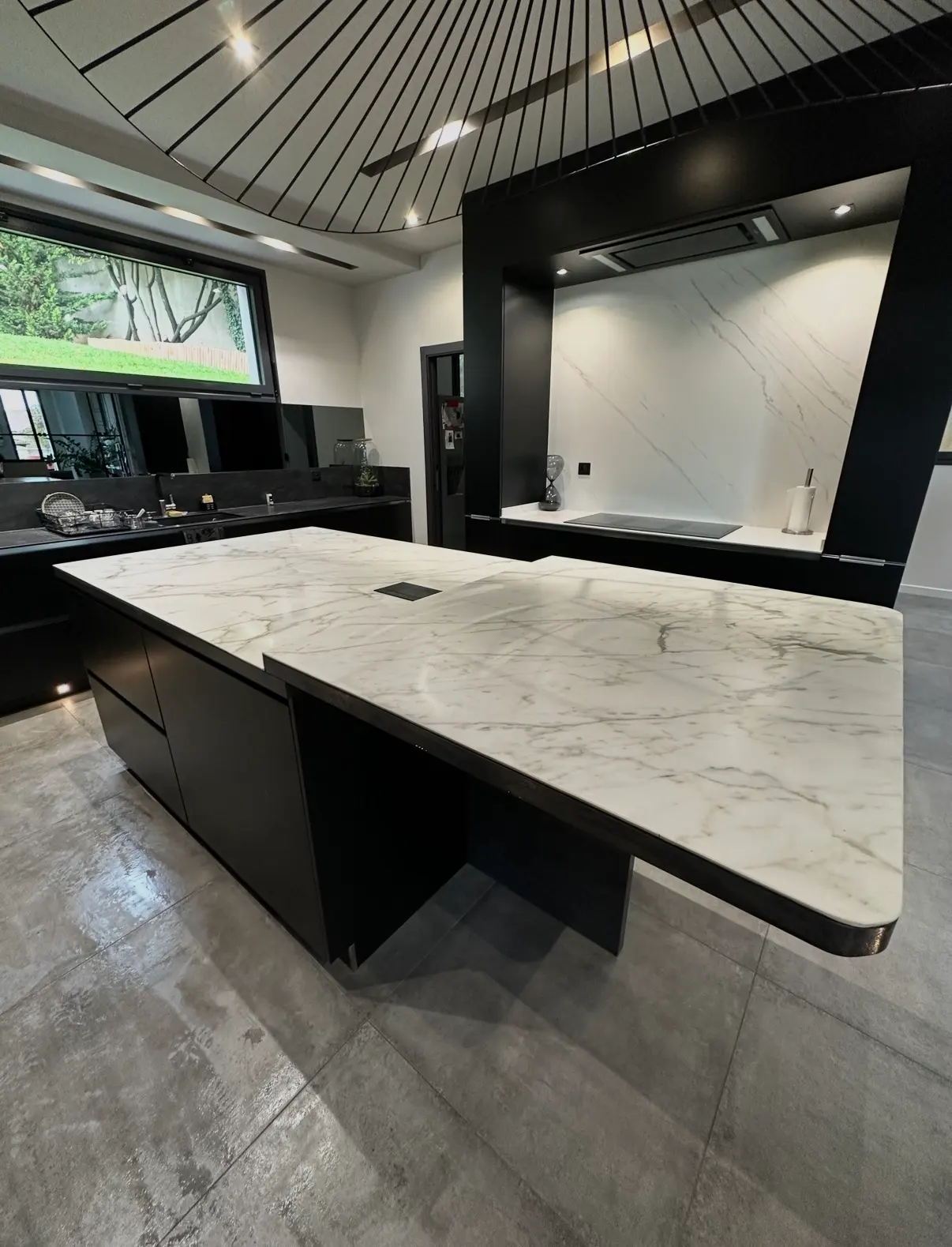 Cuisine contemporaine noire avec îlot central, crédence effet marbre blanc et sol en grands carreaux gris