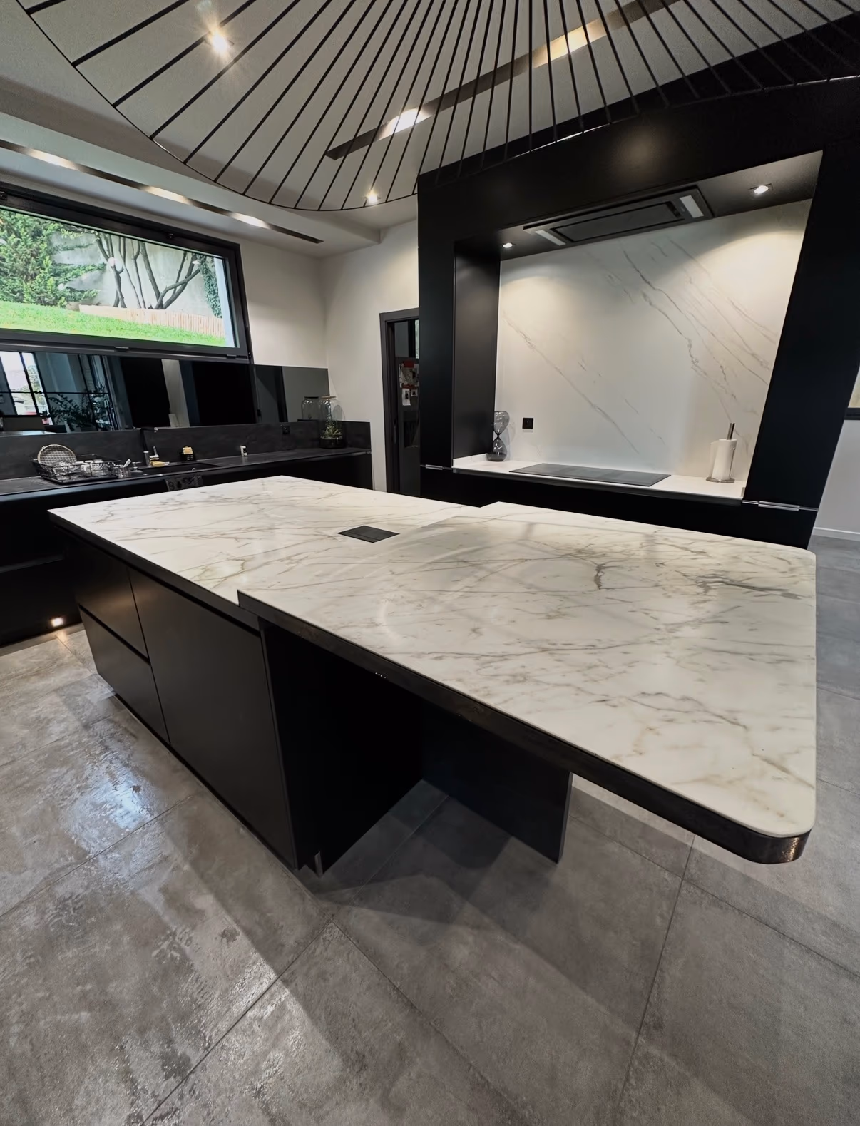 Cuisine contemporaine noire avec îlot central, crédence effet marbre blanc et sol en grands carreaux gris
