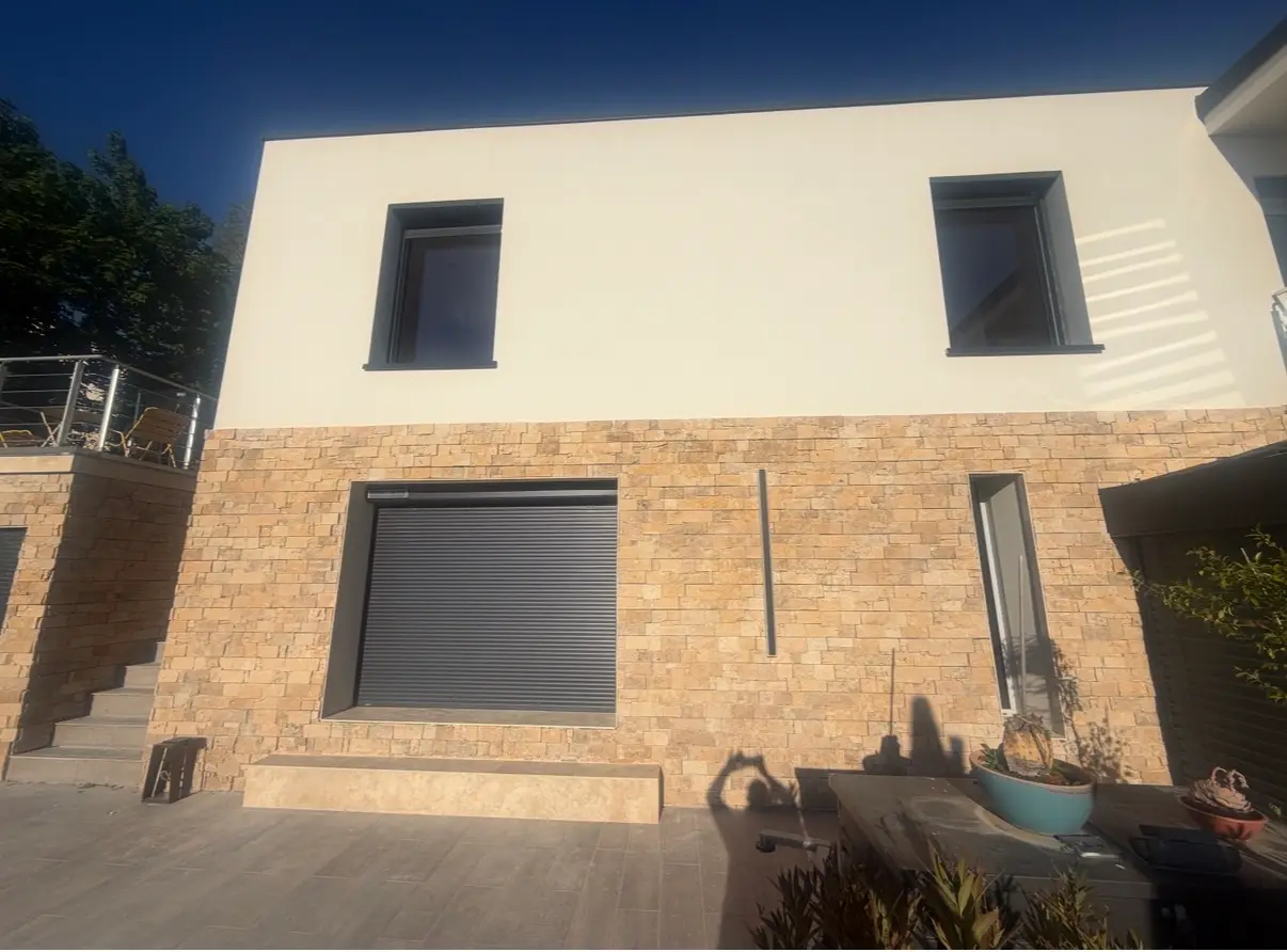 Façade contemporaine habillée de pierre naturelle avec terrasse carrelée au premier plan