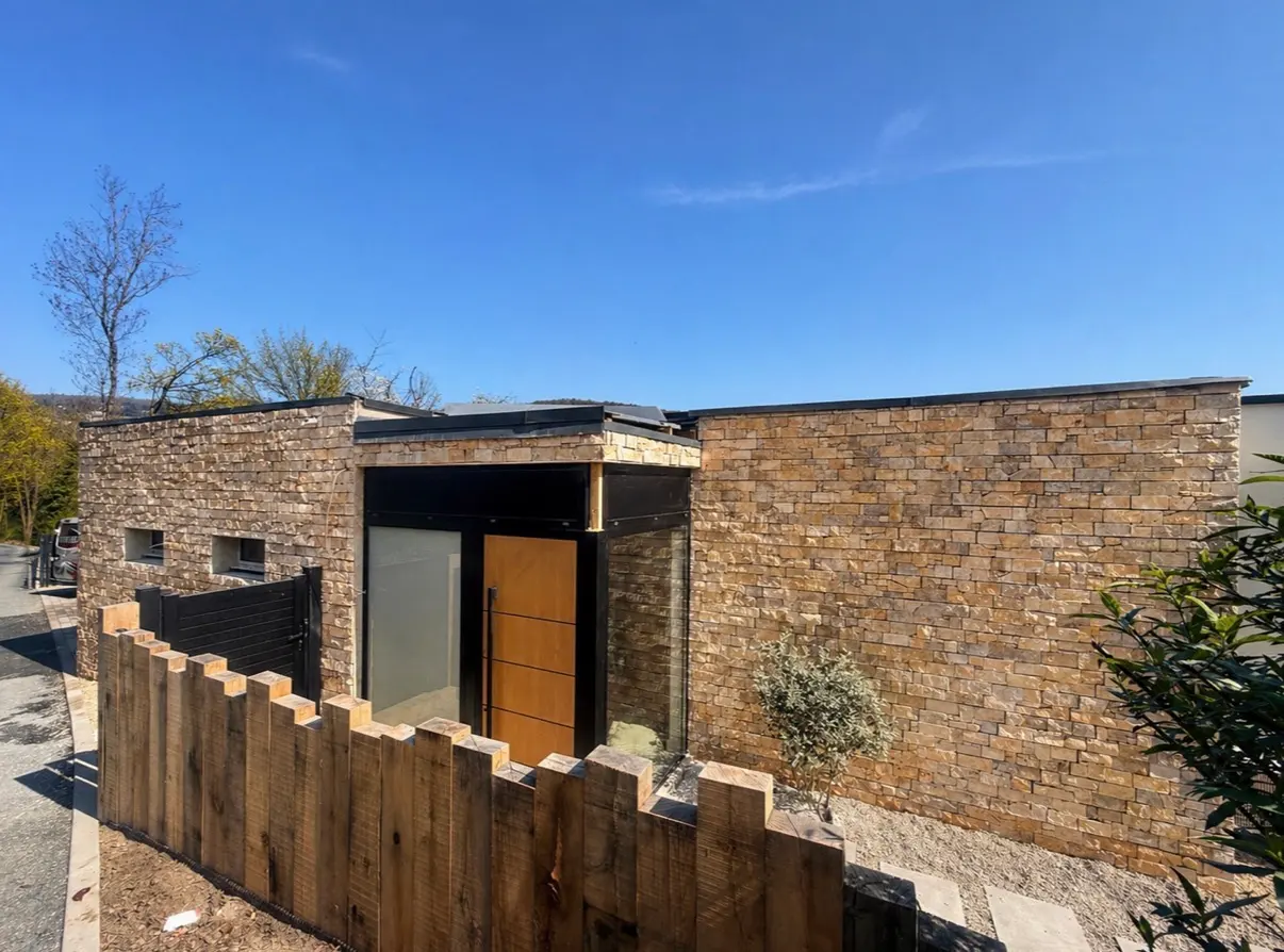 Façade contemporaine habillée de parement en pierre naturelle avec porte et clôture en bois