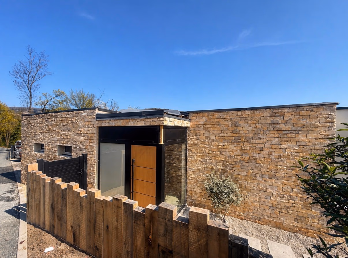 Façade contemporaine habillée de parement en pierre naturelle avec porte et clôture en bois