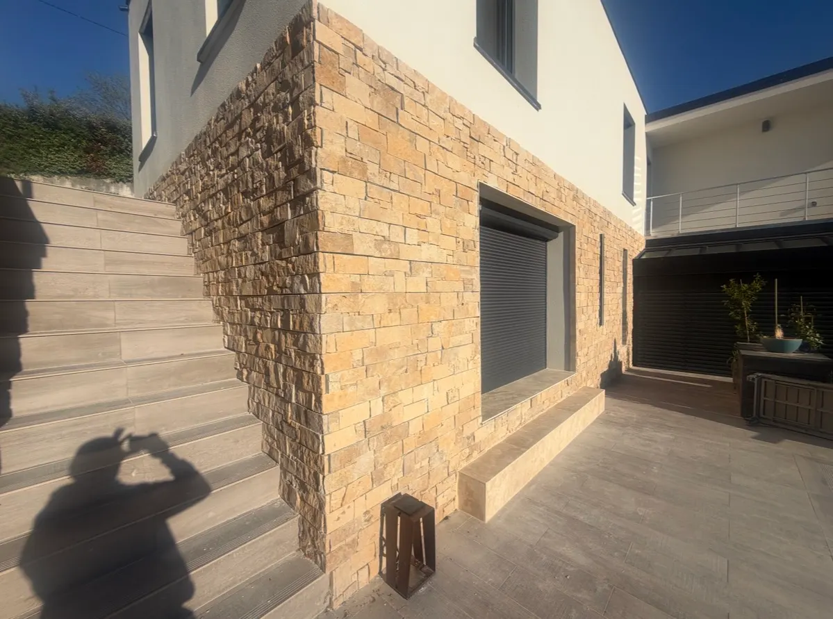 Façade en parement de pierre bordée d’un escalier et d’une terrasse carrelée