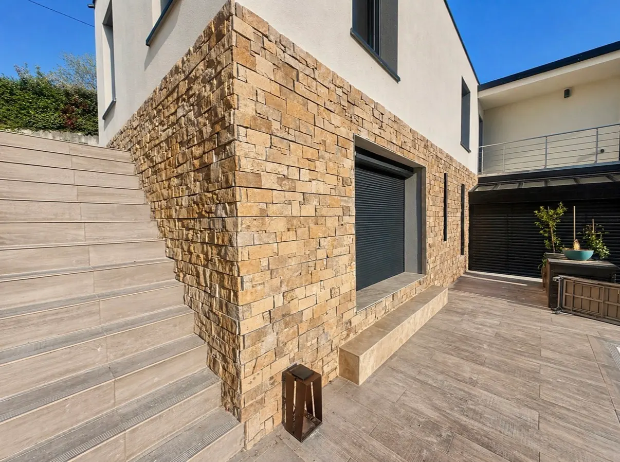 Parement en pierre naturelle sur une façade contemporaine avec terrasse et escalier carrelés