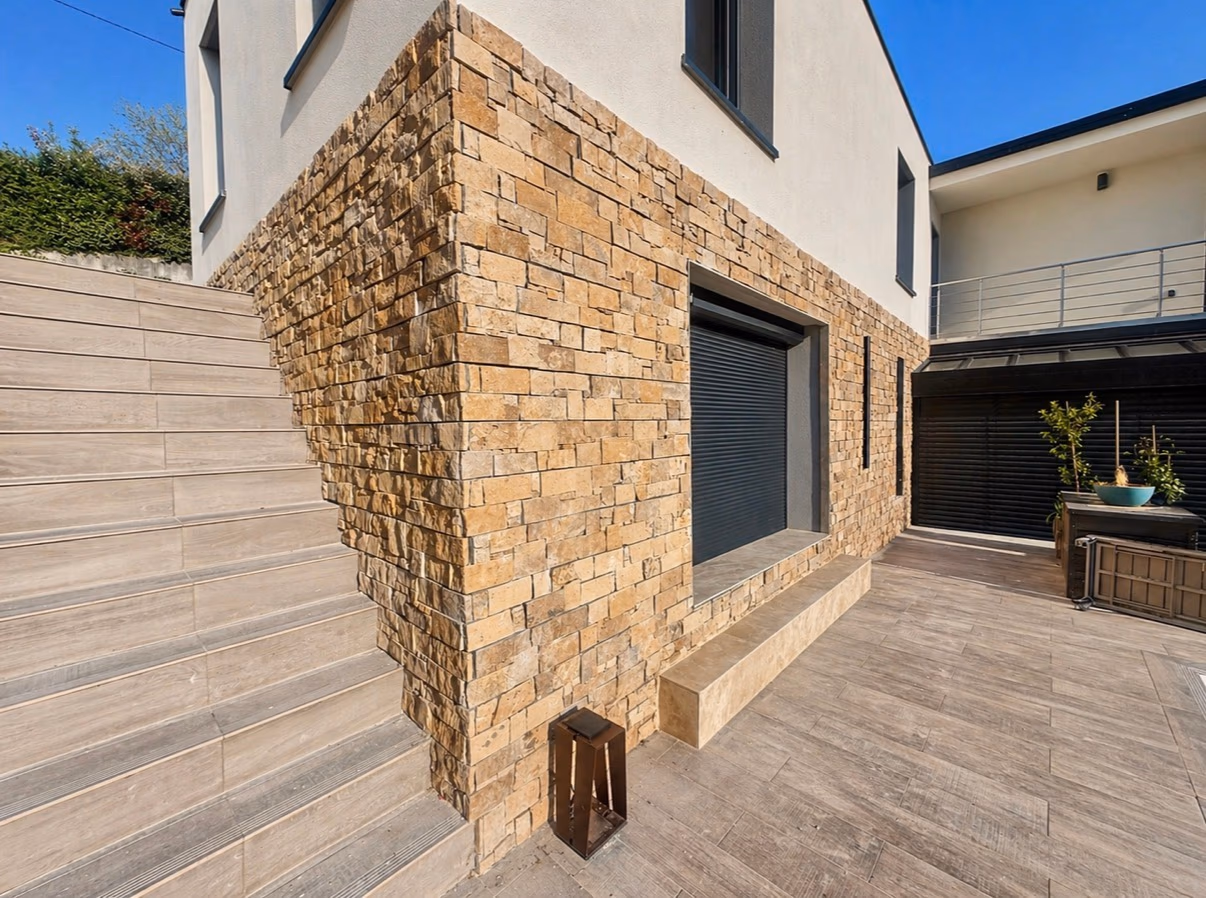 Parement en pierre naturelle sur une façade contemporaine avec terrasse et escalier carrelés