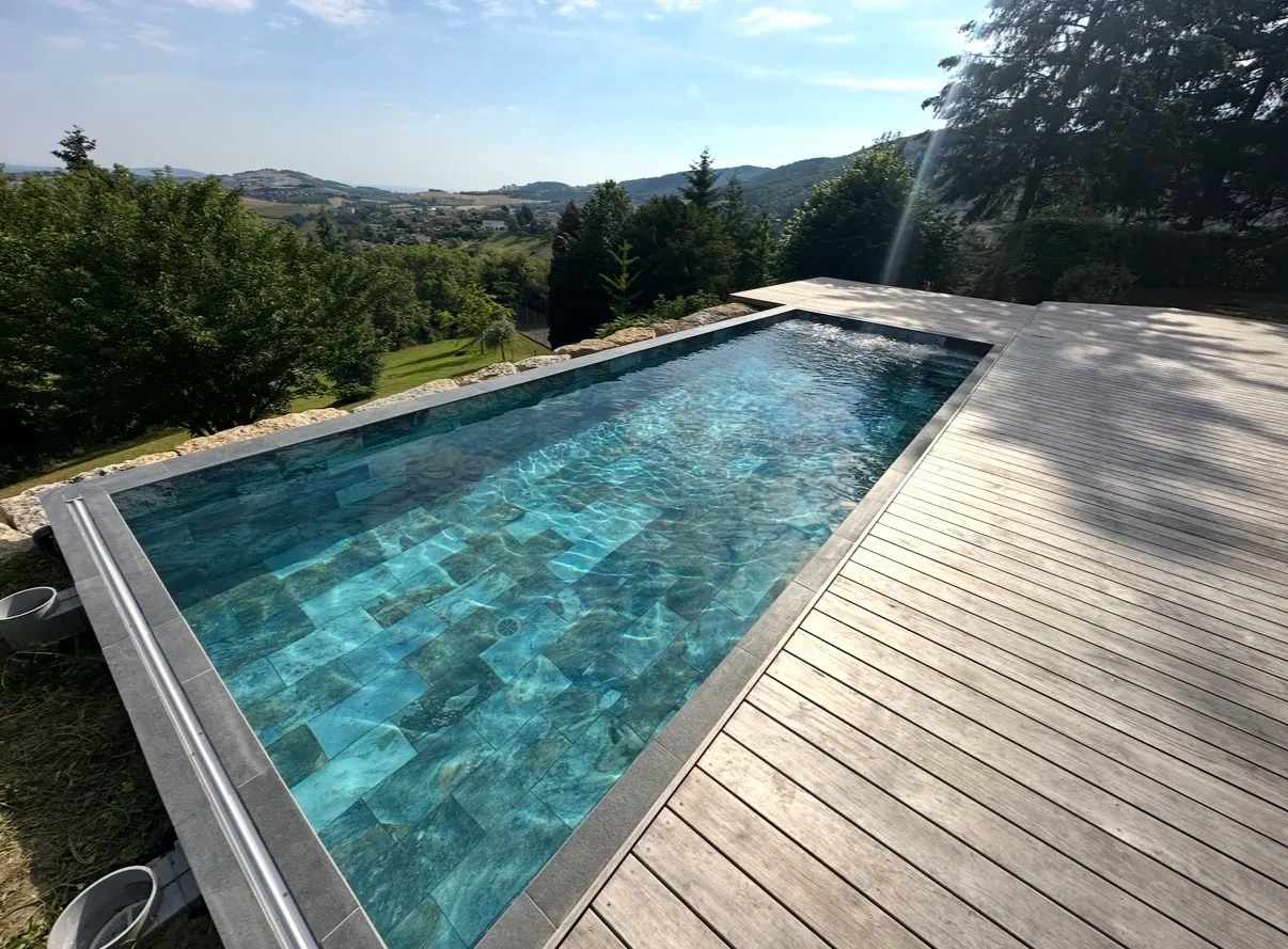 Piscine extérieure rectangulaire bordée de carrelage bleu turquoise et d’une plage en bois
