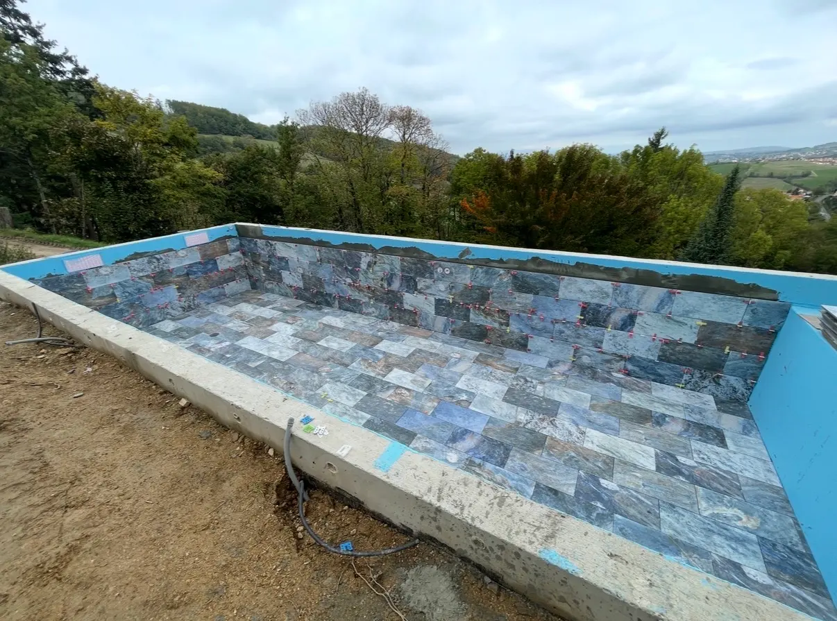 Piscine extérieure en cours de finition avec carreaux en pierre aux nuances bleutées et grises
