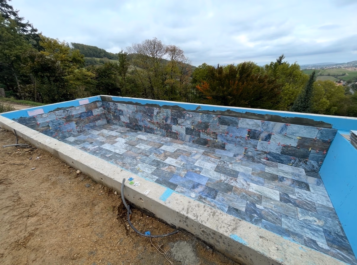 Piscine extérieure en cours de finition avec carreaux en pierre aux nuances bleutées et grises