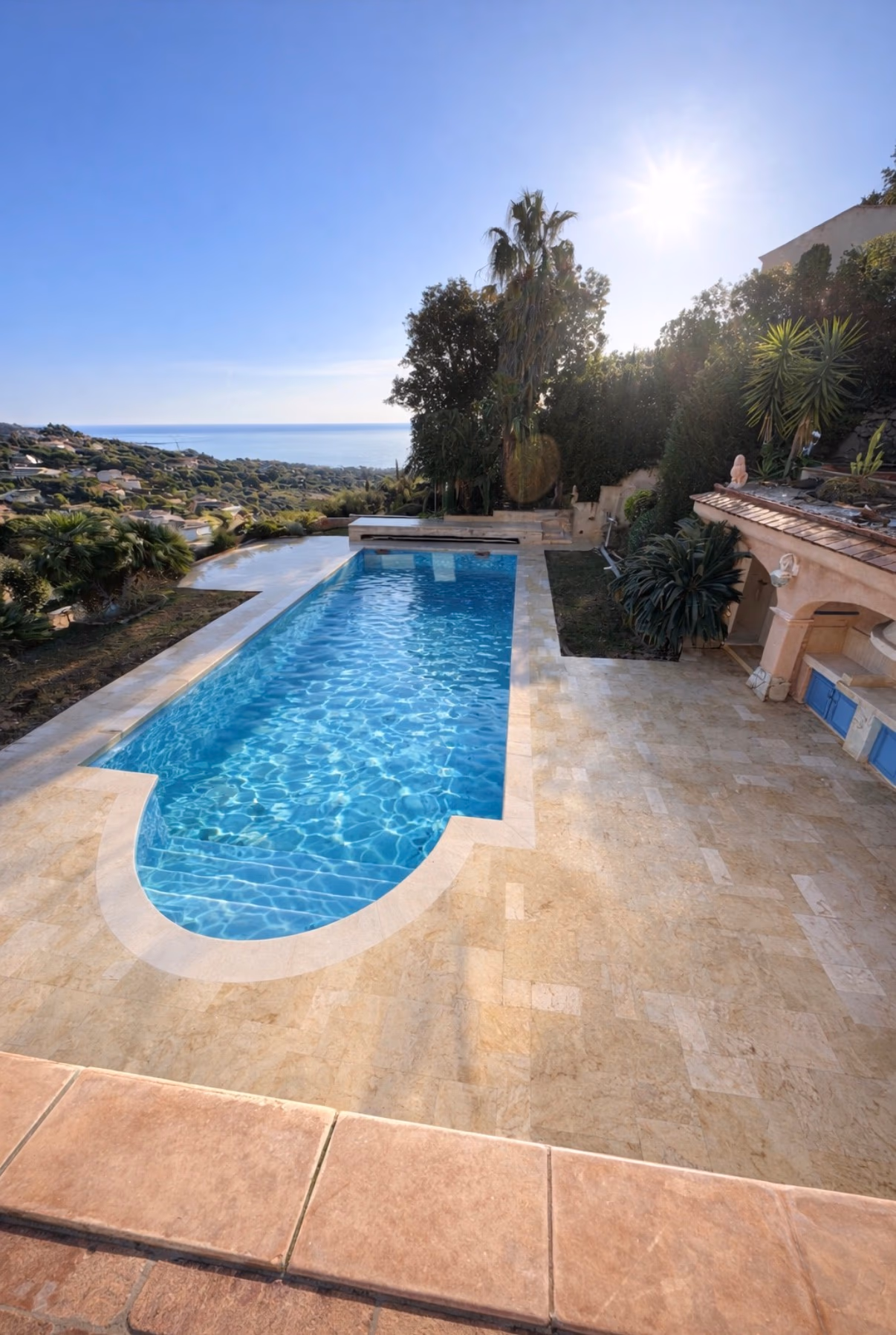 Piscine extérieure bordée de travertin clair dans un jardin avec vue sur la mer