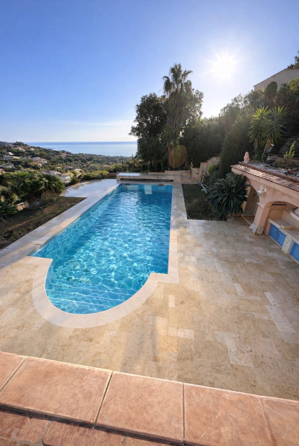 Piscine extérieure bordée de travertin clair dans un jardin avec vue sur la mer