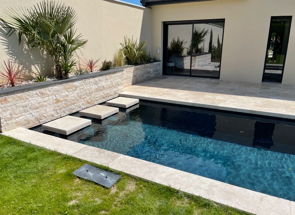 Piscine extérieure bordée d’un carrelage clair et d’une terrasse minérale avec parement en pierre