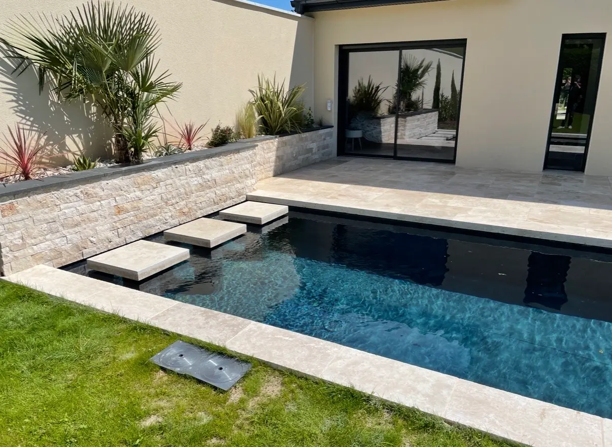 Piscine extérieure bordée de carrelage clair, d’une terrasse minérale et d’un parement en pierre