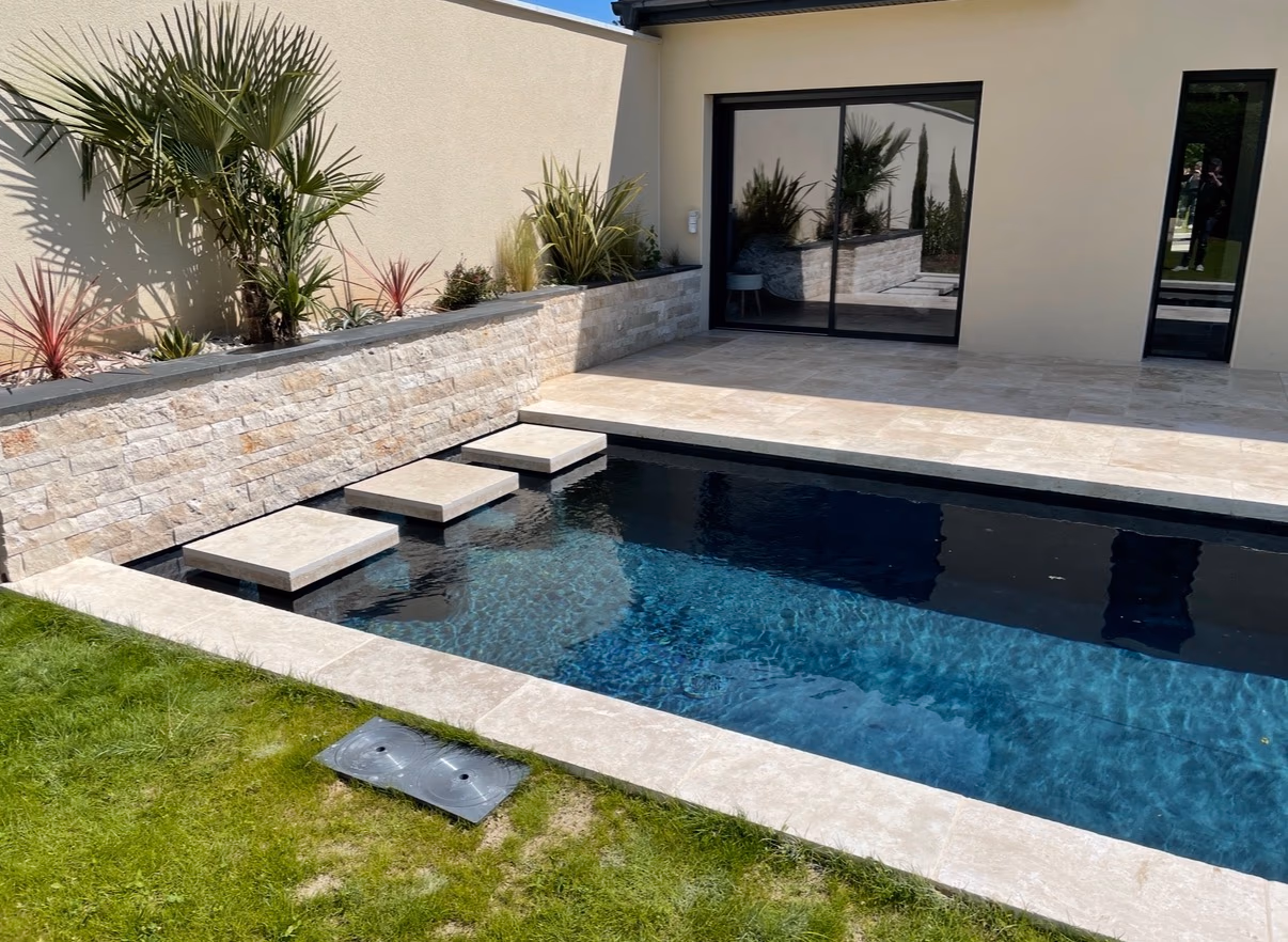 Piscine extérieure bordée d’un carrelage clair, d’une terrasse minérale et d’un parement en pierre