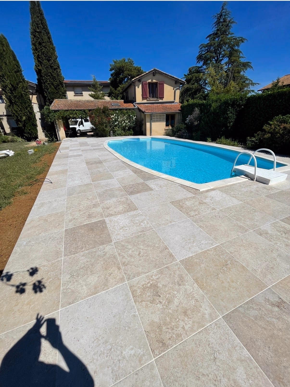 Grande terrasse en carreaux beige autour d’une piscine extérieure devant une maison