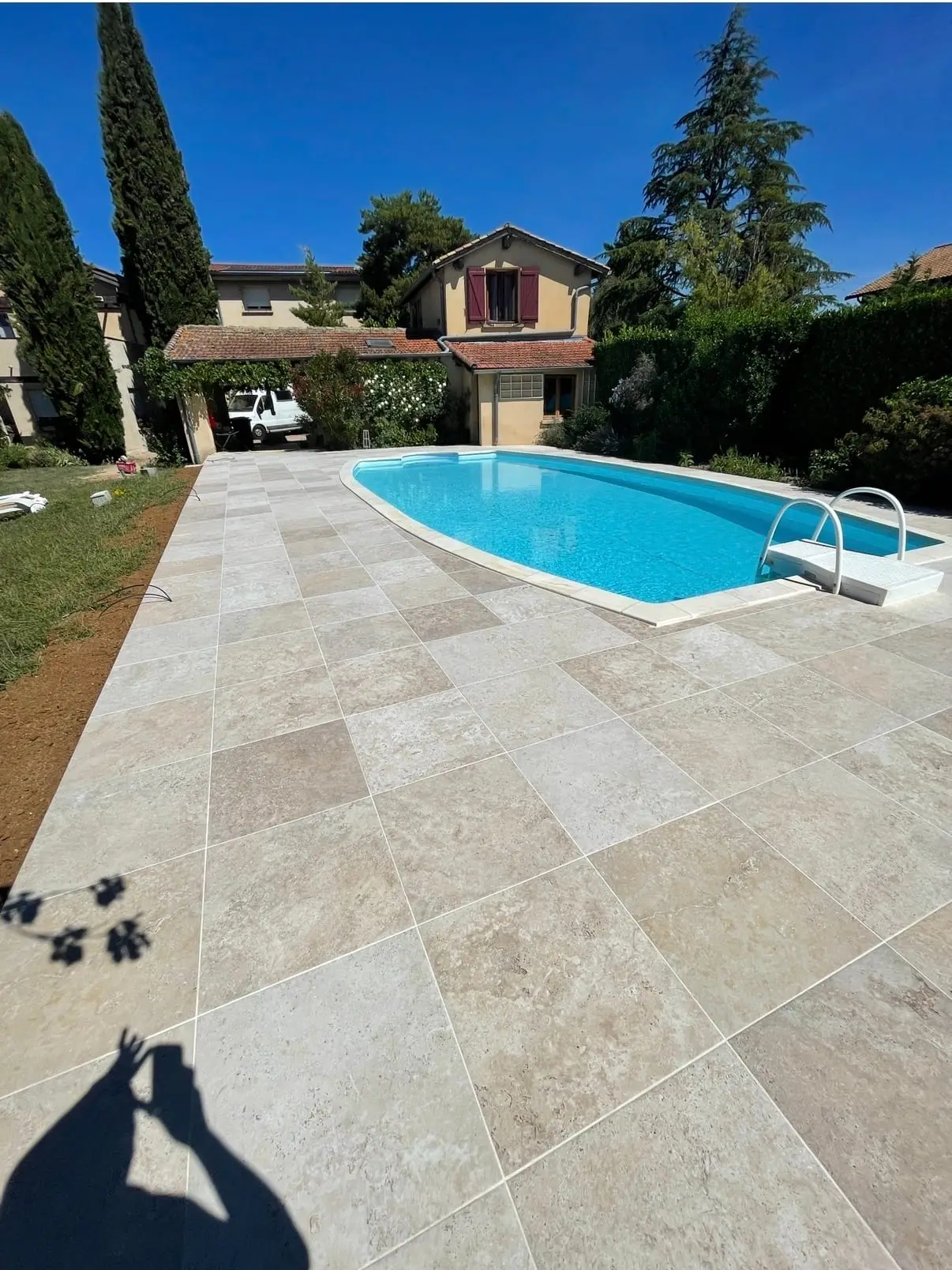Grande terrasse en carreaux beige autour d’une piscine extérieure devant une maison