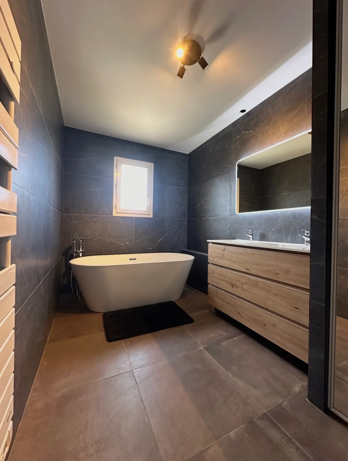 Salle de bain avec carrelage mural gris veiné, baignoire îlot et meuble double vasque en bois