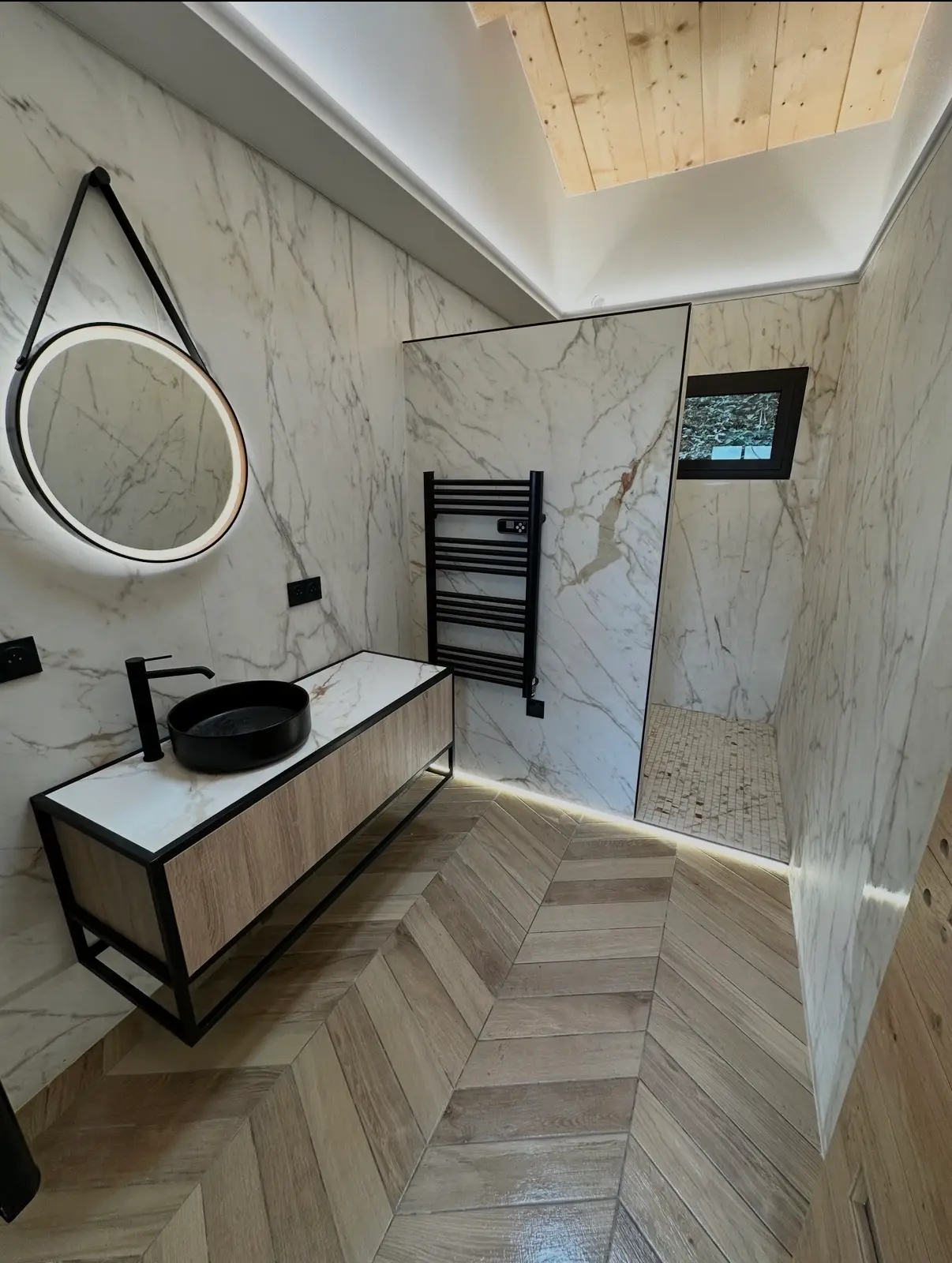 Salle de bain habillée de carrelage effet marbre avec sol imitation bois posé en chevrons