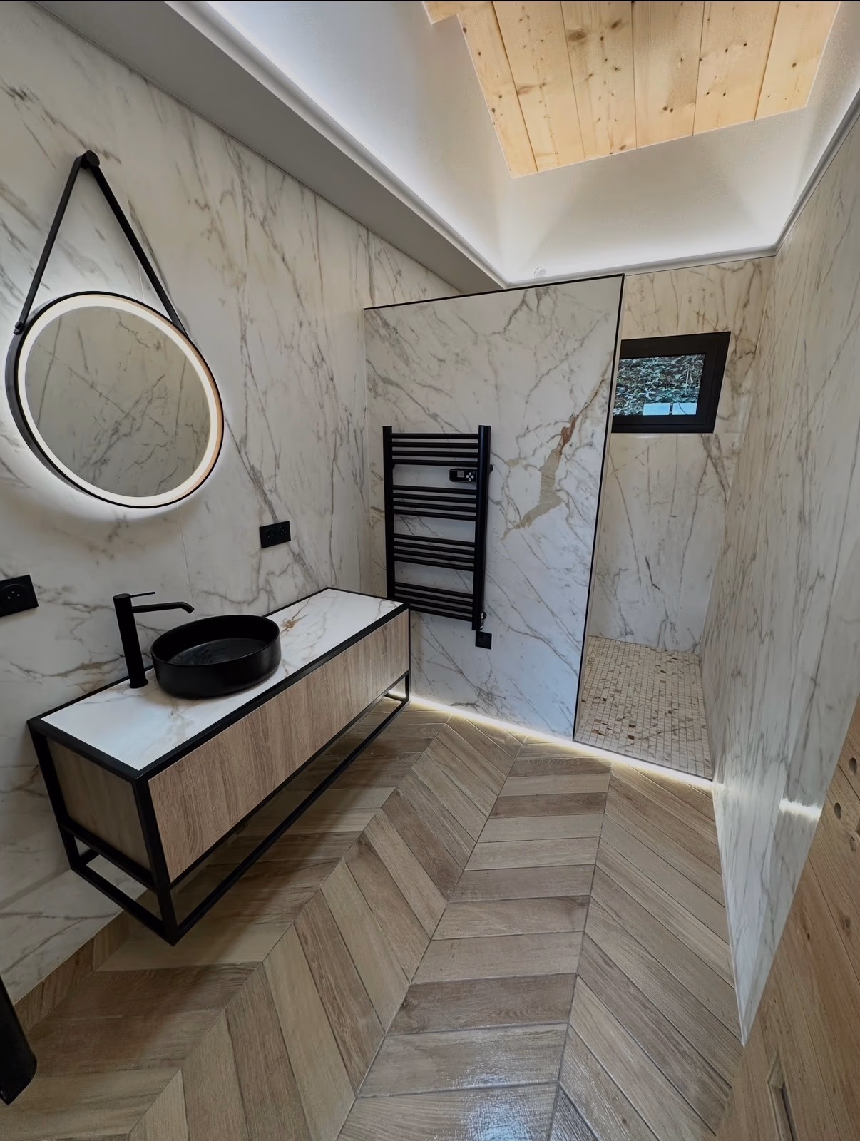 Salle de bain habillée de carrelage effet marbre avec sol imitation bois posé en chevrons