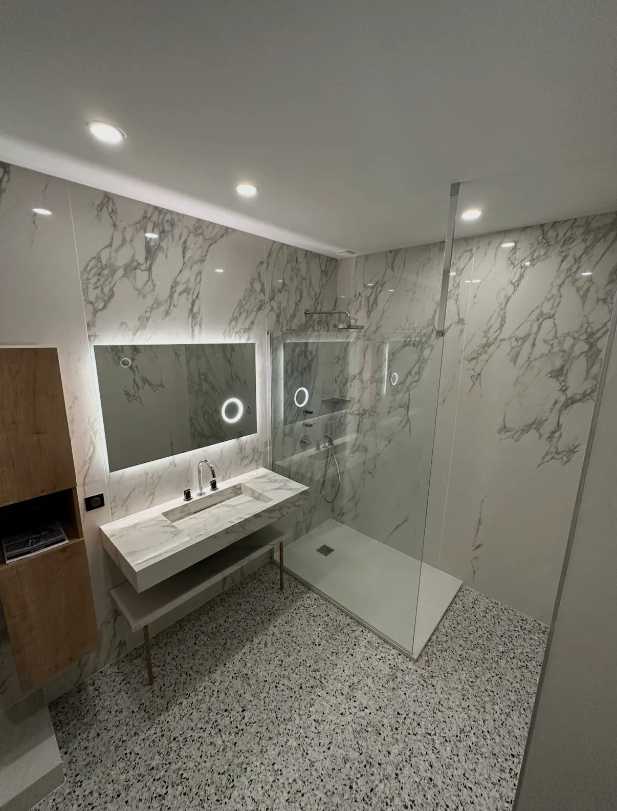 Salle de bain avec grands carreaux effet marbre, douche vitrée et sol terrazzo