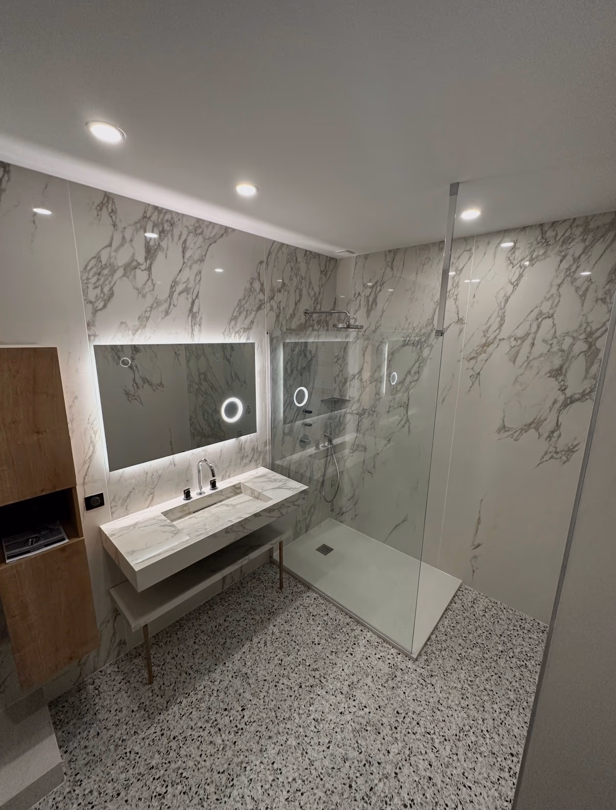 Salle de bain avec grands carreaux effet marbre, douche vitrée et sol terrazzo