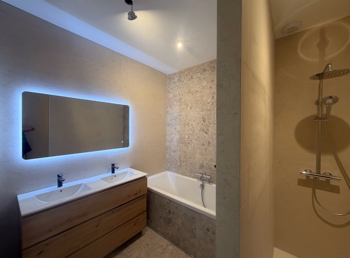 Salle de bain avec double vasque en bois, baignoire et douche habillées de pierre naturelle